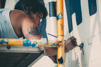 A woman on scaffolding painting a wall.