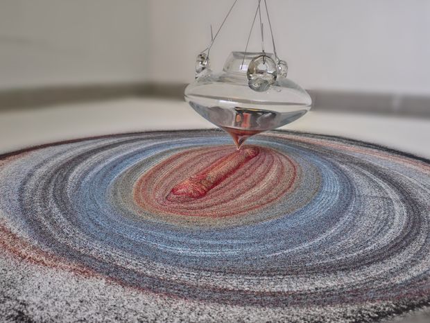 Glass pendulum creating a pattern in sand with different colors