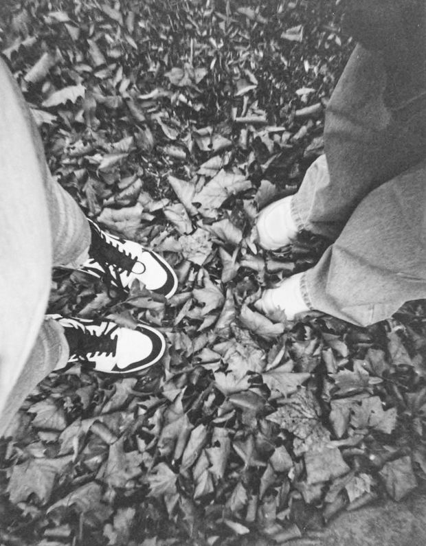 Black & white photo looking down at two pairs of feet standing on ground covered with leaves