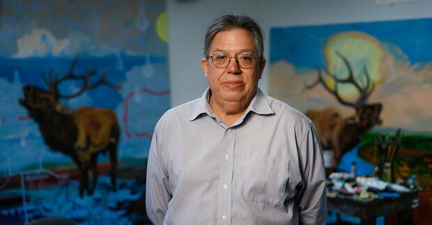 The artist in the studio is standing between two images of elk.