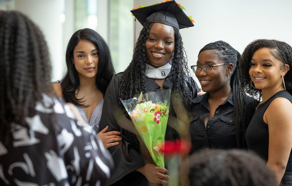 A graduate holding flowers poses for a photo with three loved ones