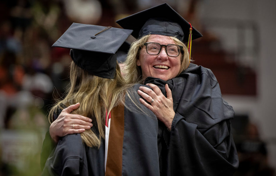 A faculty member hugs a graduate on the stage