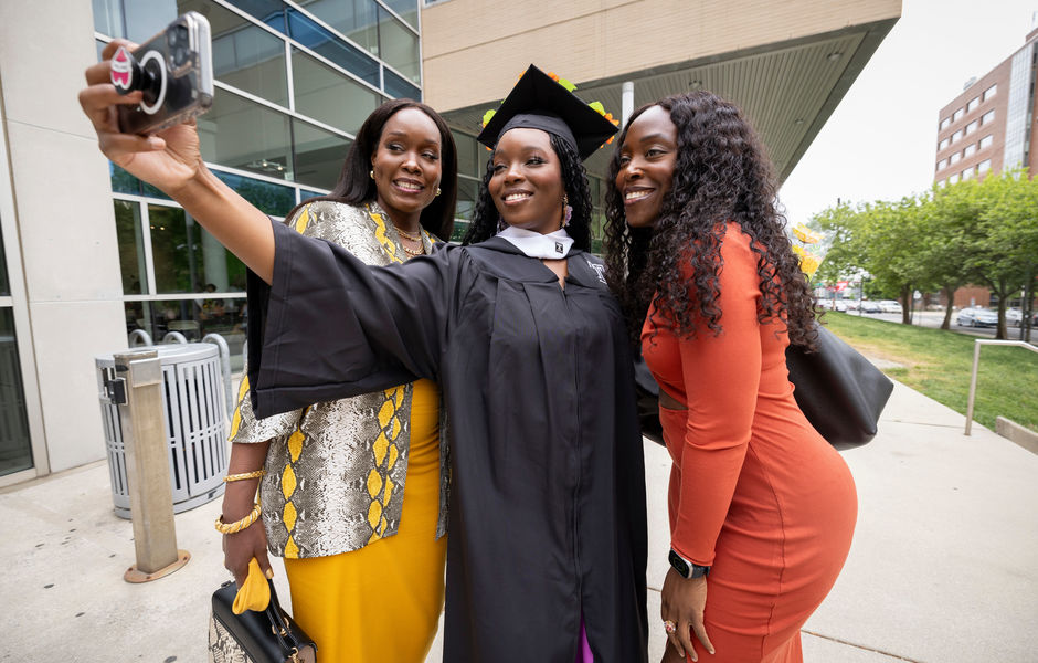 A graduate taking a selfie with two loved ones outside the Tyler building