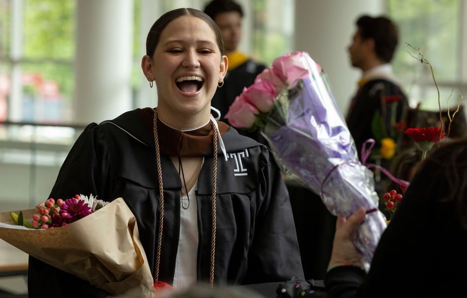 A graduate holding flowers and laughing
