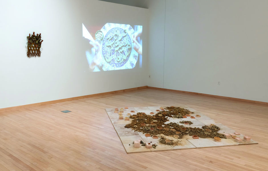 Installation view showing ceramic tiles covered in loose pigment and small ceramic pieces, tulip sculpture hanging on the wall, and a video projection on the wall