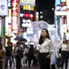 Woman on a busy street in Tokyo holding a clear umbrella at night