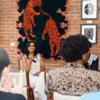 Sahiti Bonam seated with a microphone with artwork in the background, speaking to a group of people