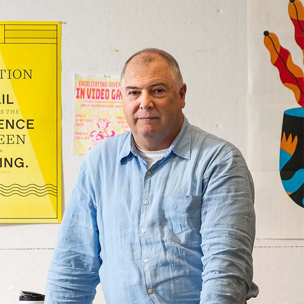  Dermot MacCormack, wearing a blue shirt, stands in a design studio at Tyler, looking at the camera.