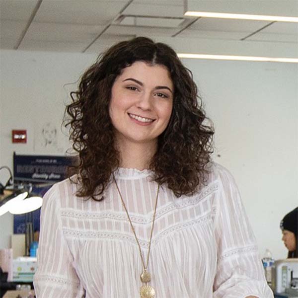 Mia Culberston stands in a Tyler design studio, holding a book in her hands and smiling at the camera.